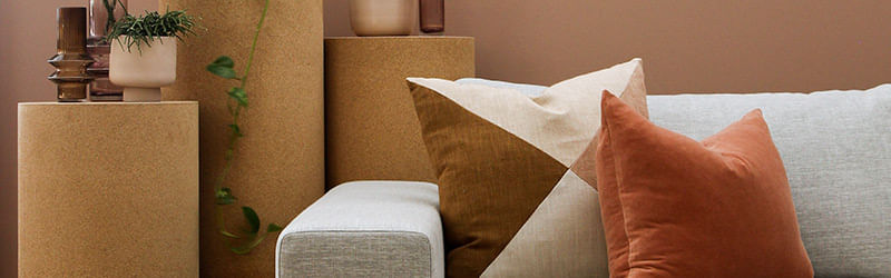 Almofadas nas cores laranja e bege posicionadas sob sofá na cor cinza ao lado de móveis
decorativos.