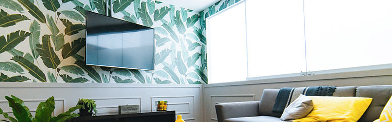 Sala de televisão com papel de parede estampado com folhas verdes.