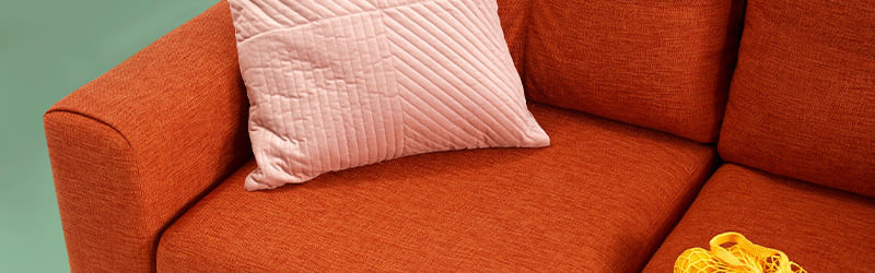 Sofá de dois lugares em tom laranja com almofada rosa sob ele.